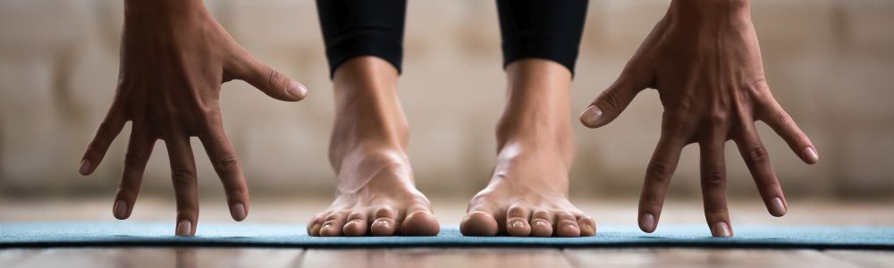 Titelbild Entspannung & Bewegung: Hände neben Füßen von stehender Person auf Gymnastikmatte